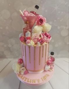 a pink and gold birthday cake with flowers on the top is decorated with liquor bottles, roses, and confetti