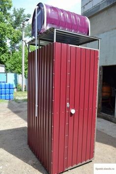 a red portable toilet sitting on top of a dirt ground next to a building and trees