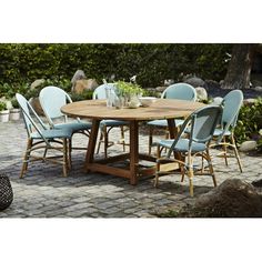 a wooden table with blue chairs around it on a brick patio surrounded by greenery