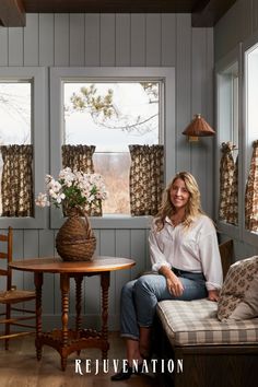 a woman sitting on a bench next to a table with flowers in the window sill