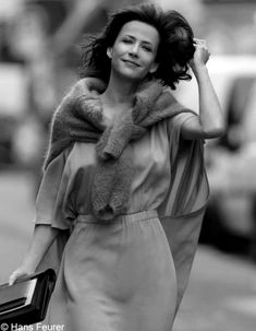 a woman walking down the street in a dress and fur stole around her neck, carrying a briefcase