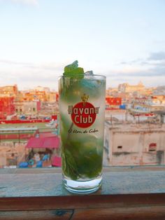 a glass filled with green liquid sitting on top of a wooden table next to a cityscape