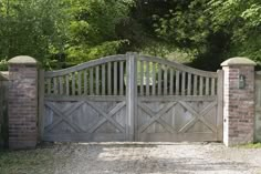 a wooden gate with brick pillars in front of a stone wall and tree lined driveway