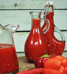 two bottles of sauce sit on a table with peppers, tomatoes and other ingredients around them