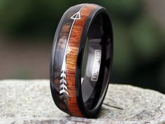 a black ceramic ring with an arrow inlay and wood inlay, on top of a rock