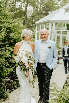 a bride and groom walking down a path in front of a glasshouse at their wedding