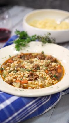 two bowls of soup are sitting on a blue and white table cloth, one bowl is filled with food