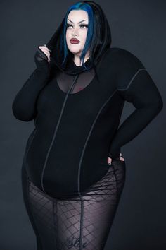 a woman with blue hair and black bodysuit posing for a photo in front of a dark background