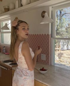 a woman standing in a kitchen with a bowl of strawberries on the counter next to her