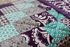 a close up of a patchwork quilt on a tablecloth with purple and teal colors