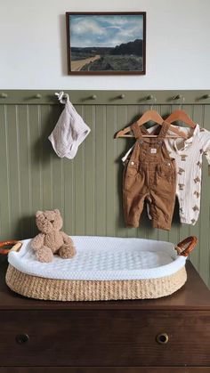 a teddy bear sitting on top of a bed next to clothes hanging from the wall