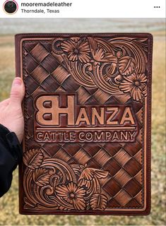 a person holding up a leather book with the words ghanza cattle company on it