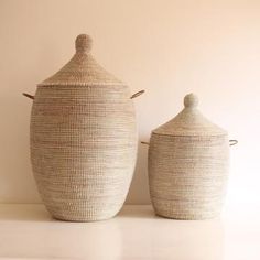 two woven baskets sitting next to each other on a white counter top, one has a lid and the other has a handle