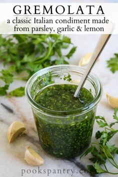 a jar filled with pesto sauce next to lemons and parsley