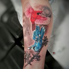 a tattoo with a red bird on it's arm and blue hand holding an object