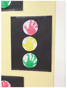 handprints on black paper are displayed in front of a yellow wall with three different colored circles