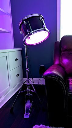 a purple light shines on the floor next to a leather chair and drum set