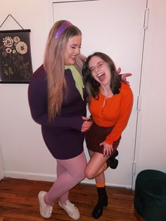 two women dressed in costumes pose for the camera while one holds her leg up and laughs