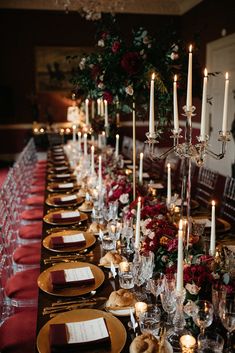 a long table is set with gold plates and red napkins, candles, and flowers