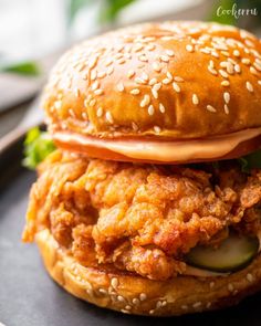 a chicken sandwich with lettuce and tomato slices on it, sitting on a black plate