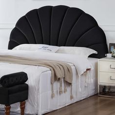 a bed with a black headboard and foot stool in a white walled room next to a wooden floor