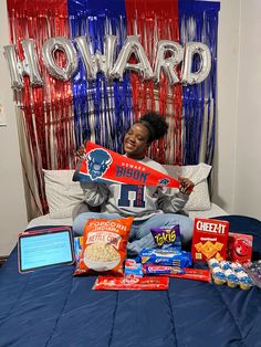 a woman laying in bed with snacks and candy on her stomach, holding up a football jersey