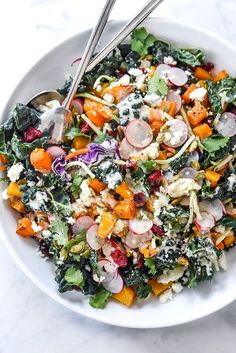 a white bowl filled with salad and two serving spoons