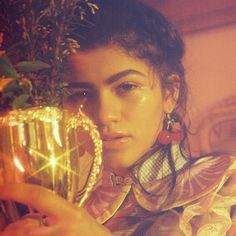 a woman holding a vase with flowers in it and looking at the camera while wearing earrings