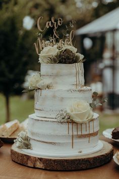 a three tiered cake with white flowers and gold lettering that says carpo machel