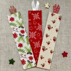 three christmas bookmarks are lined up next to each other on a linen surface with red and green decorations