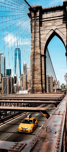 a yellow taxi cab driving across a bridge in front of the manhattan cityscape