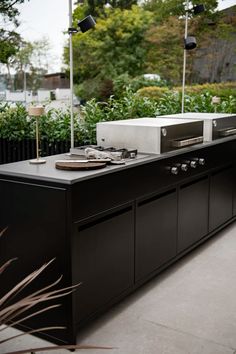 an outdoor kitchen with black cabinets and lights on the outside wall, surrounded by plants