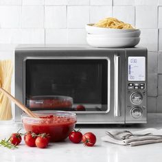 a microwave with spaghetti and tomatoes on the counter