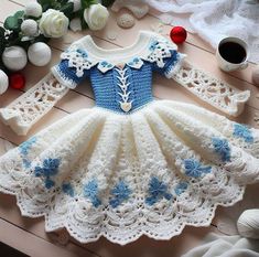 a crocheted dress with blue flowers on the bottom and white trimmings