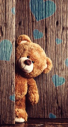 a brown teddy bear is peeking out from behind a wooden paneled wall and leaning on it's side