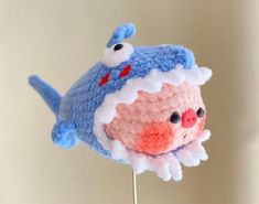 a crocheted blue and white stuffed animal on a toothpick with two eyes