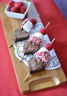 some brownies and raspberries are on a wooden tray with toothpicks