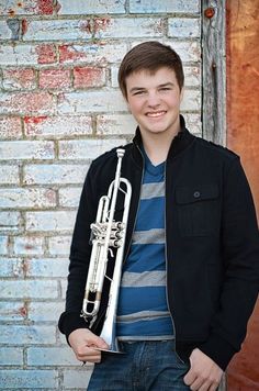 a young man holding a trumpet in front of a brick wall and smiling at the camera