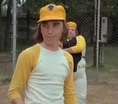 a young man standing in front of a fence wearing a yellow hat and holding a baseball bat