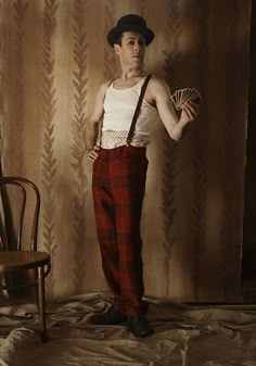 a man with a hat and suspenders standing in front of a chair