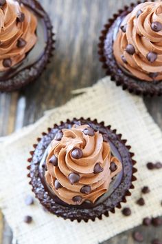 three cupcakes with chocolate frosting and chocolate chips on a napkin next to each other