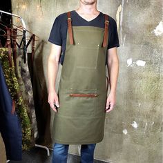 a man standing in front of a wall wearing an olive green apron with brown leather straps