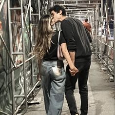 a man and woman kissing in front of a metal structure with other people standing around