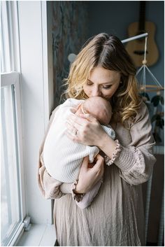 a woman holding a baby in her arms and looking out the window at something outside