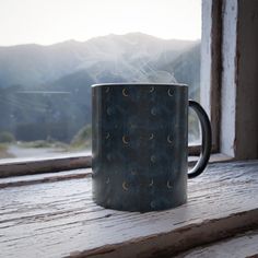 a coffee mug sitting on top of a window sill with the moon and stars painted on it