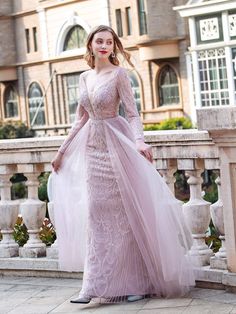 a woman in a pink gown standing on a balcony with her hands behind her back