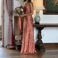 a woman in a pink dress holding a bouquet of flowers standing next to a couch