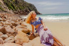 a woman sitting on rocks at the beach looking up into the sky with her eyes closed