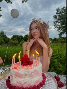 a woman sitting in front of a cake with candles on it and raspberries