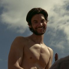 a man with no shirt standing in front of a blue sky and cloud filled sky